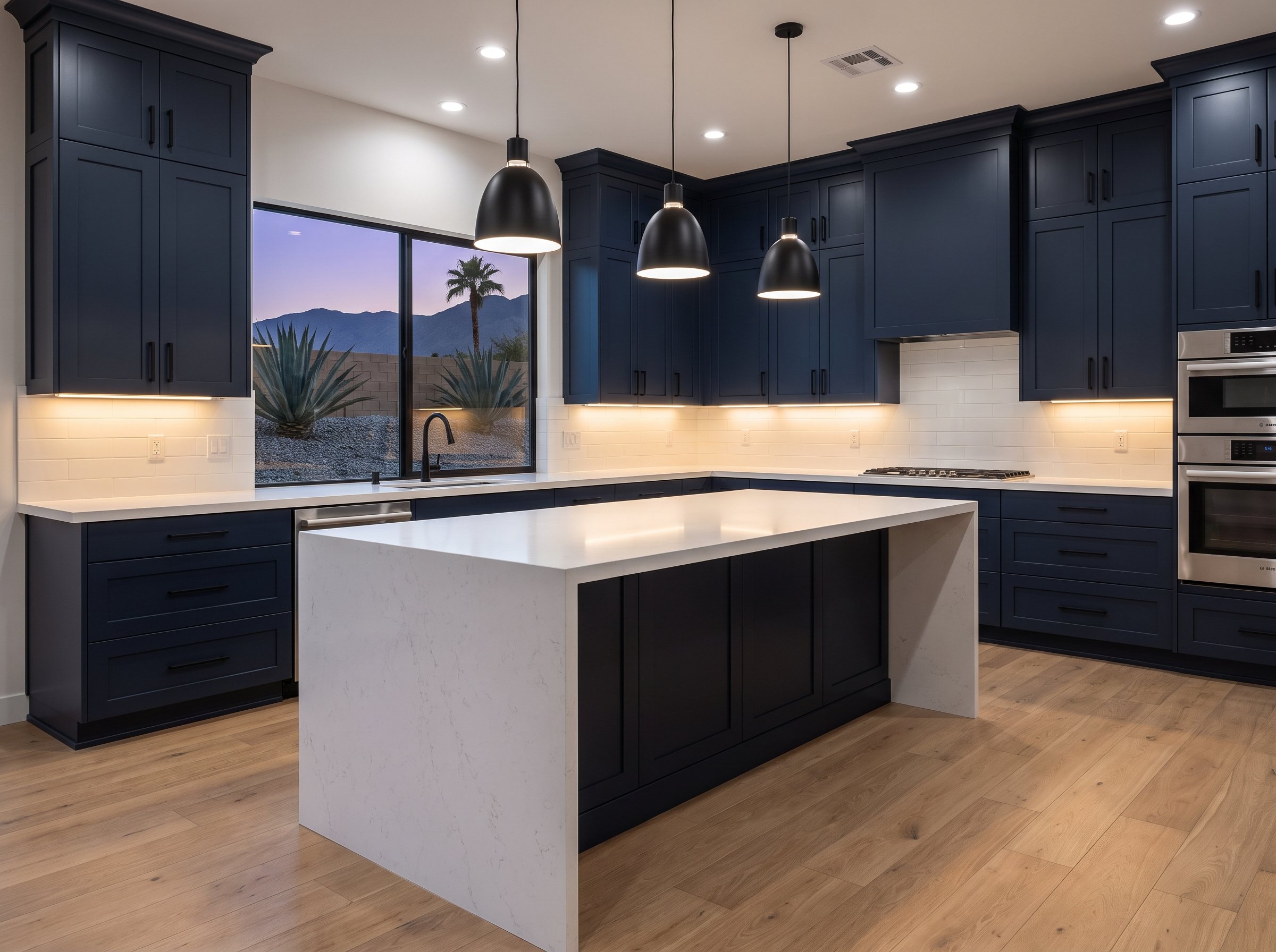 Kitchen remodel in a Las Vegas home with navy shaker cabinets, a white quartz waterfall island, subway tile backsplash, under-cabinet lighting and black pendant lights