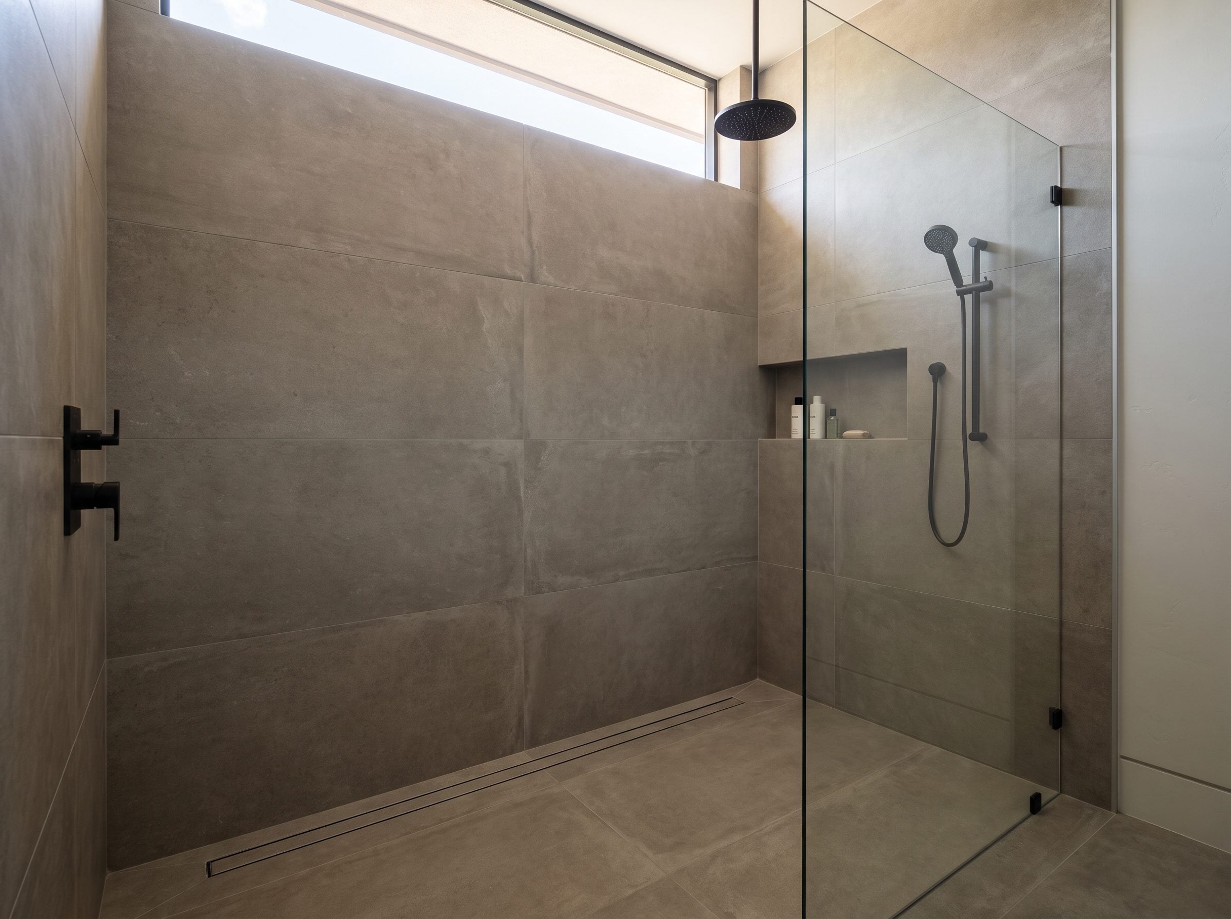 Walk-in shower in a Las Vegas home with frameless glass, large gray porcelain tile and black fixtures, the surfaces where hard water shows first